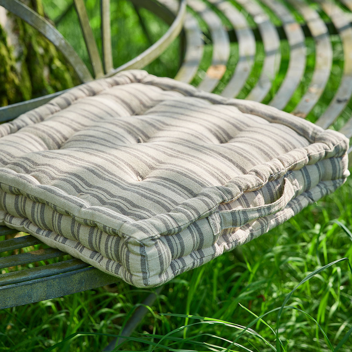 Charcoal ticking stripe box cushion on a curved iron garden bench