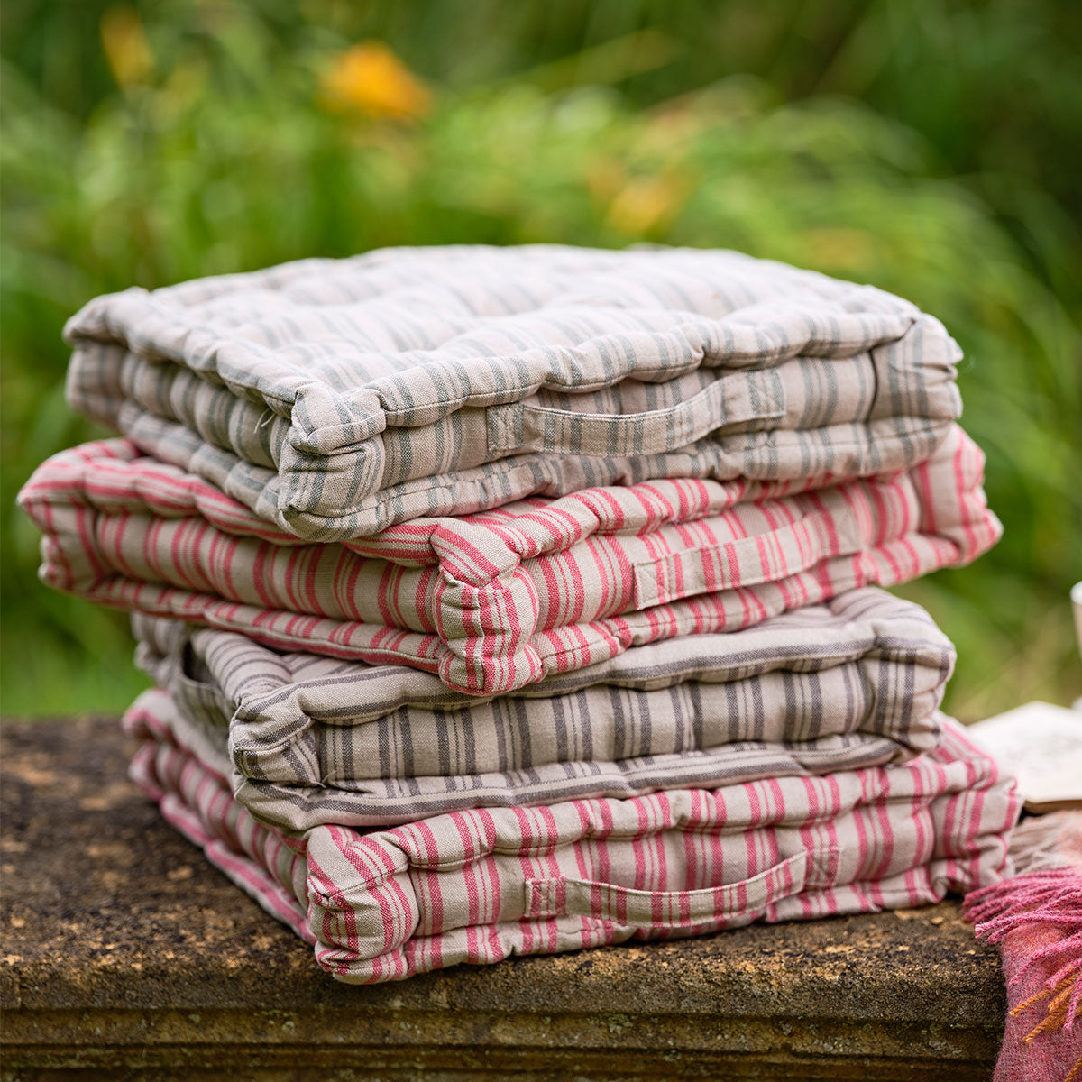 Red and natural ticking stripe box cushions stacked on a garden table