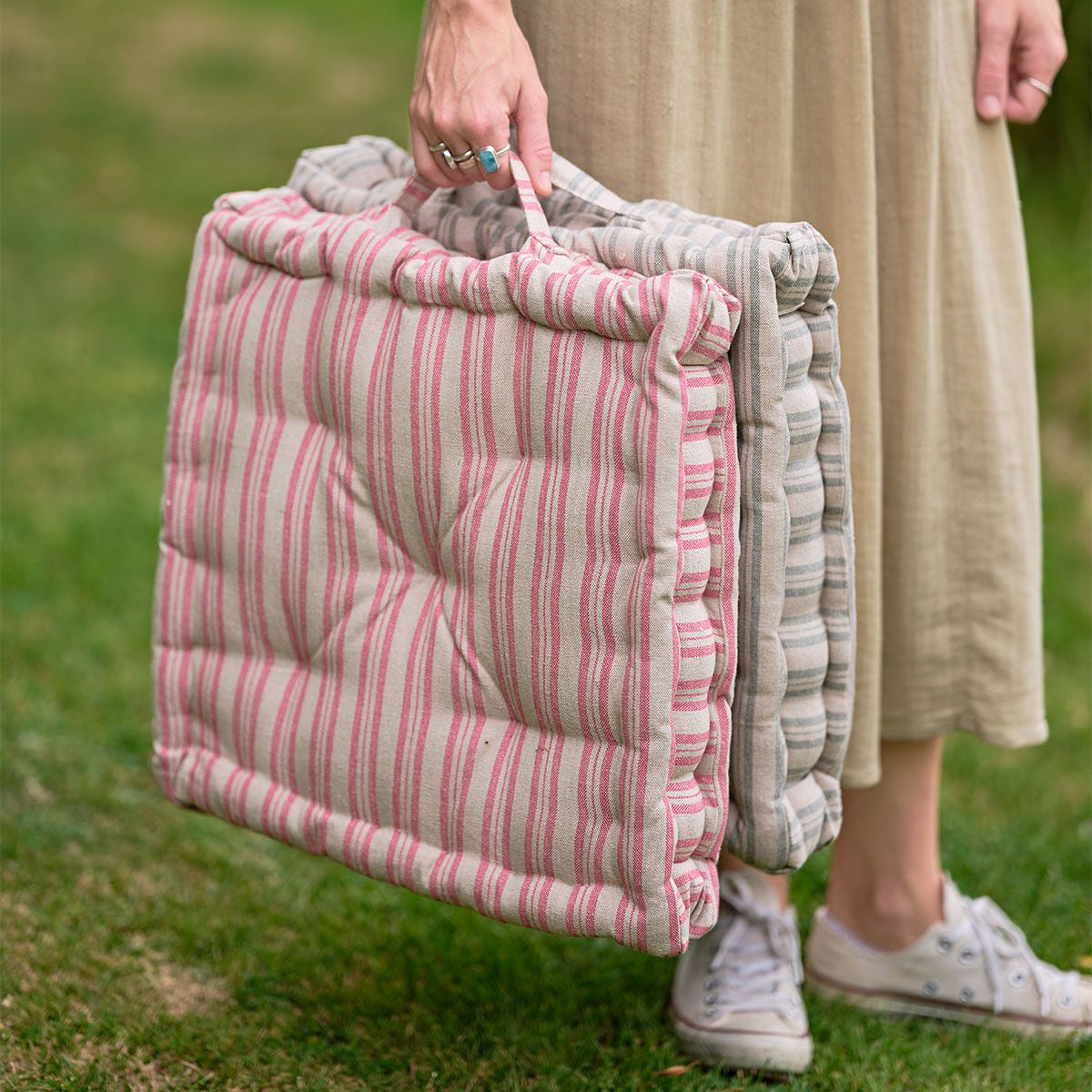 Woman carrying two striped box cushions by their handles across a lawn