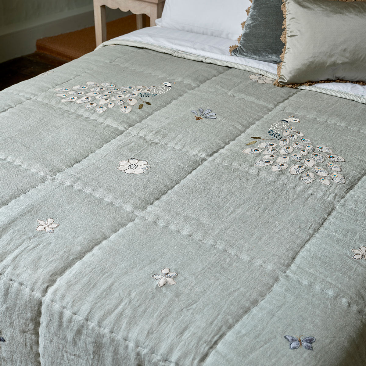 Celadon embroidered peacocks linen quilt spread across a made bed
