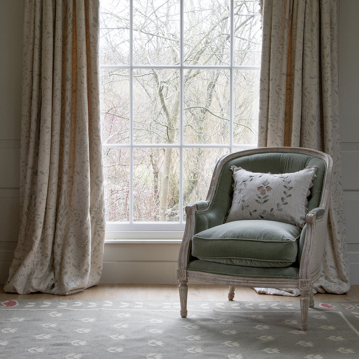 Large buttoned green velvet library chair beside a curtained window