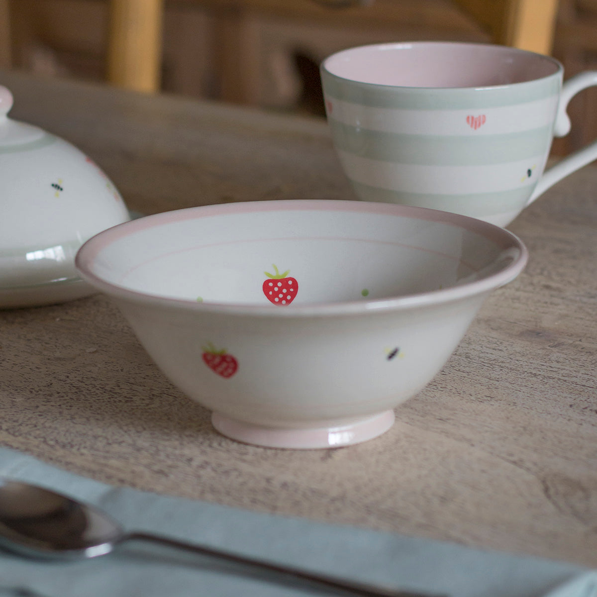 Strawberry pudding bowl nested among hand-painted cups and a teapot