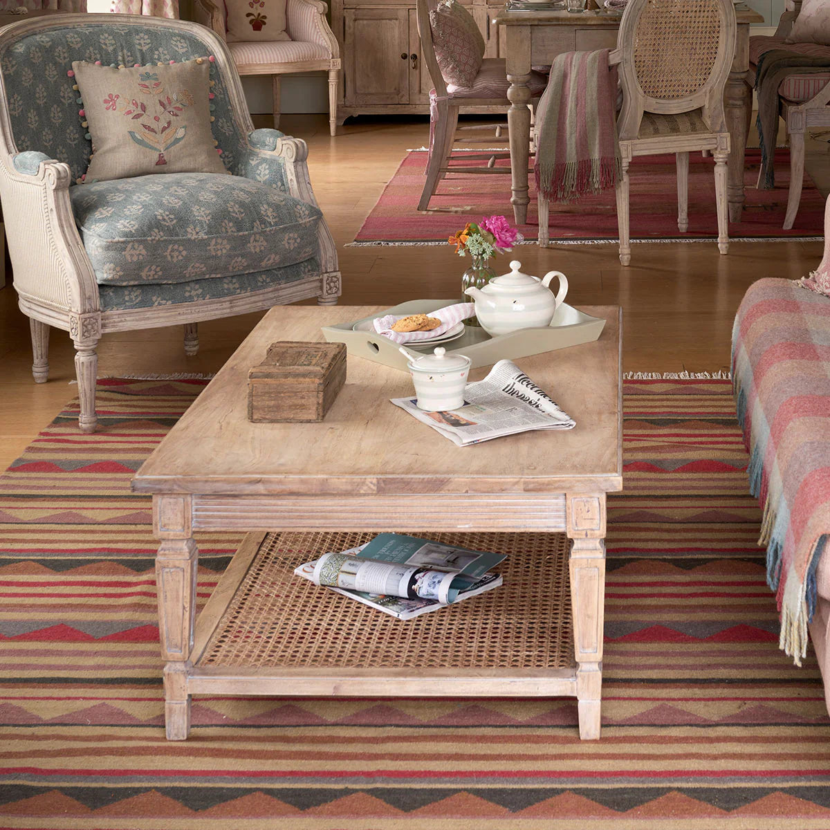 Caned coffee table with a tea tray in a sitting room over a striped kilim