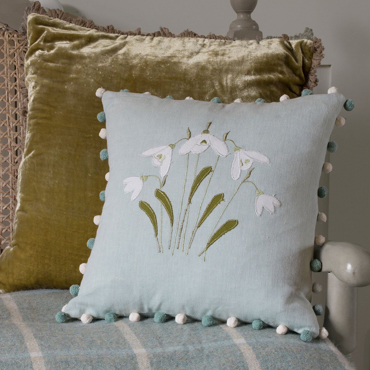 Snowdrop cushion beside an olive velvet cushion on a wooden bench