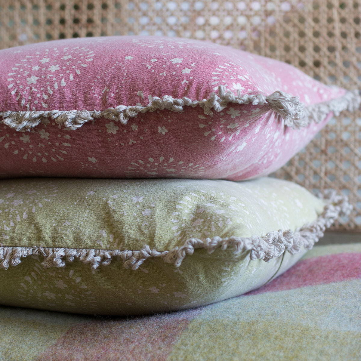 Close view of the fringed edge on stacked Lullaby cushions in rose and olive