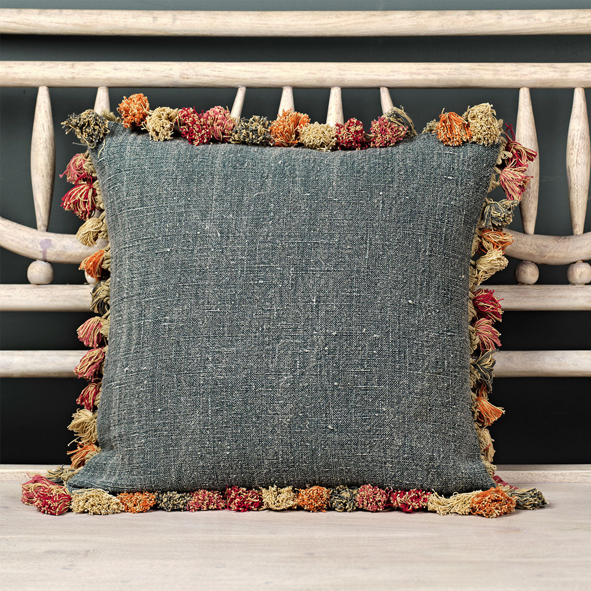 Faded indigo rustic linen cushion with a multicoloured tassel trim on a bench