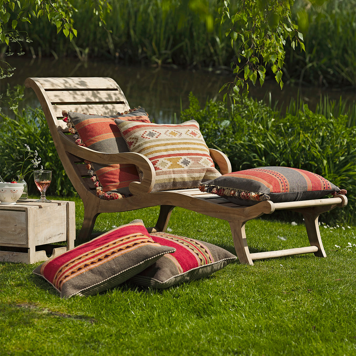 Wooden steamer lounger piled with striped cushions beside still water