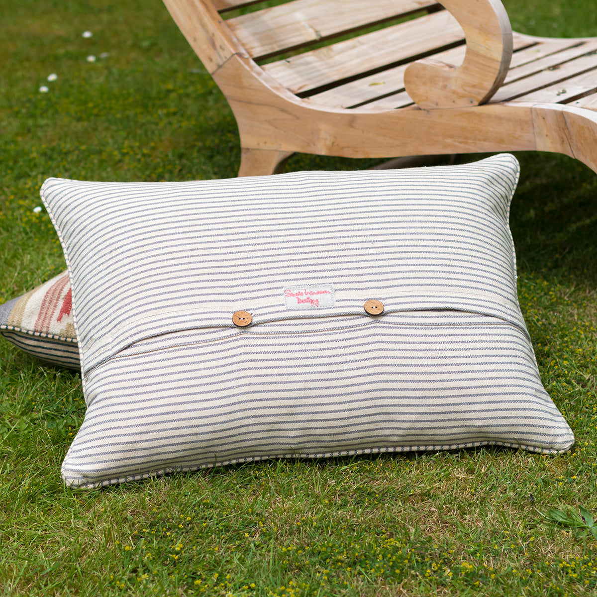 Reverse of the kilim cushion in striped ticking with wooden buttons, on grass