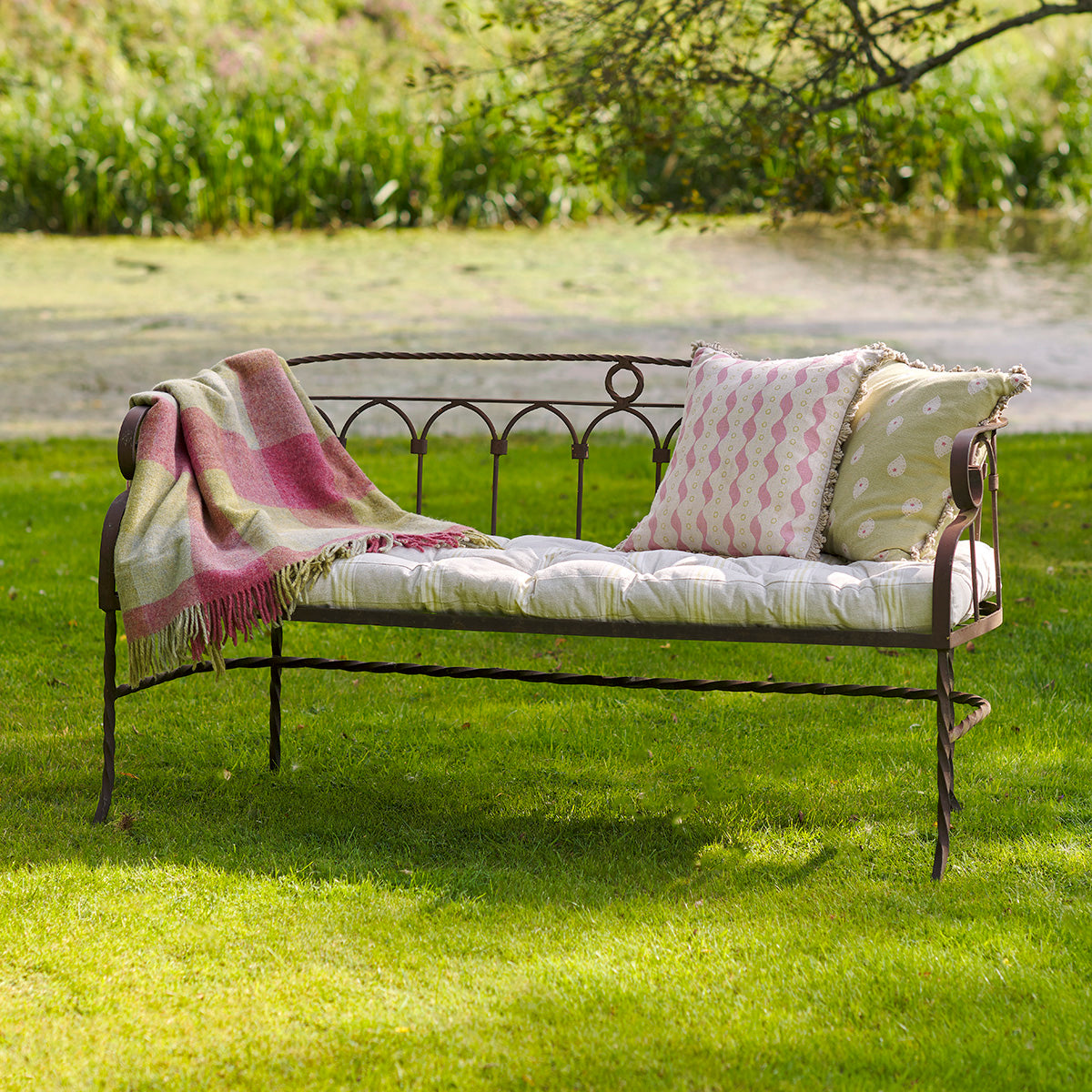 Metal garden bench with striped box cushion and pink throw on a lawn