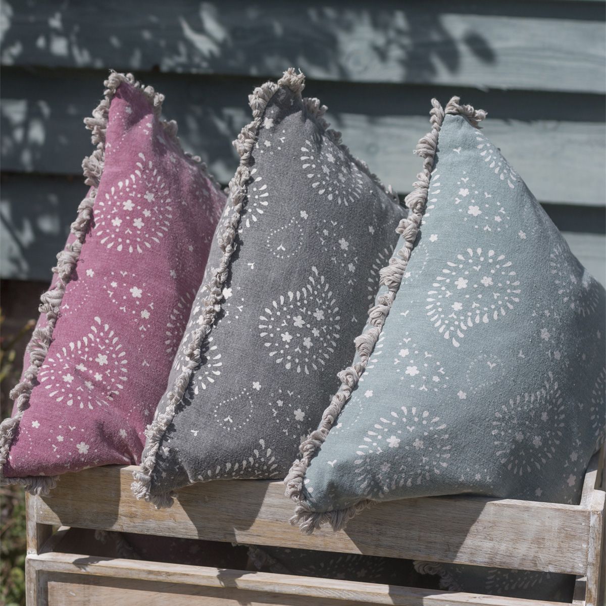 Three Lullaby cushions in pink, charcoal and duck egg propped outdoors
