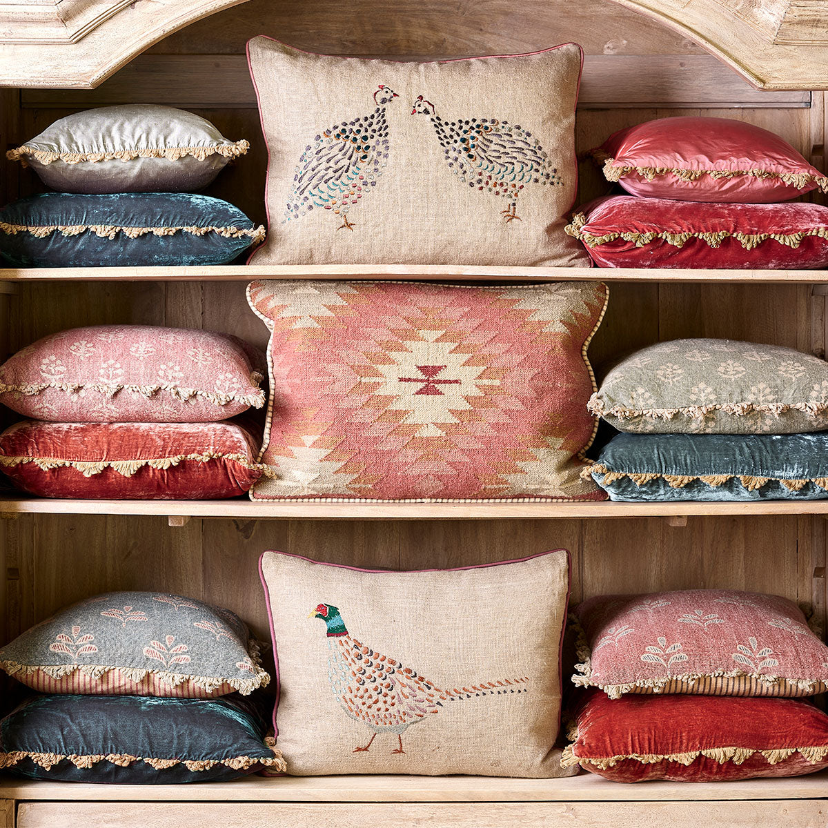 Dresser shelves stacked with red, pink and blue cushions including reverse leaf linen