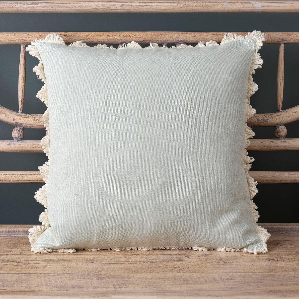Duck egg plain cotton cushion with fringed edge on a caned bench
