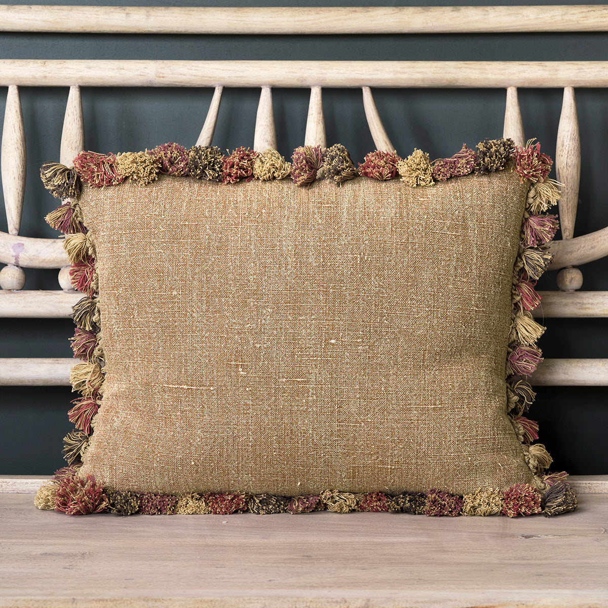 Saffron rustic linen cushion edged with tassels against a painted bench