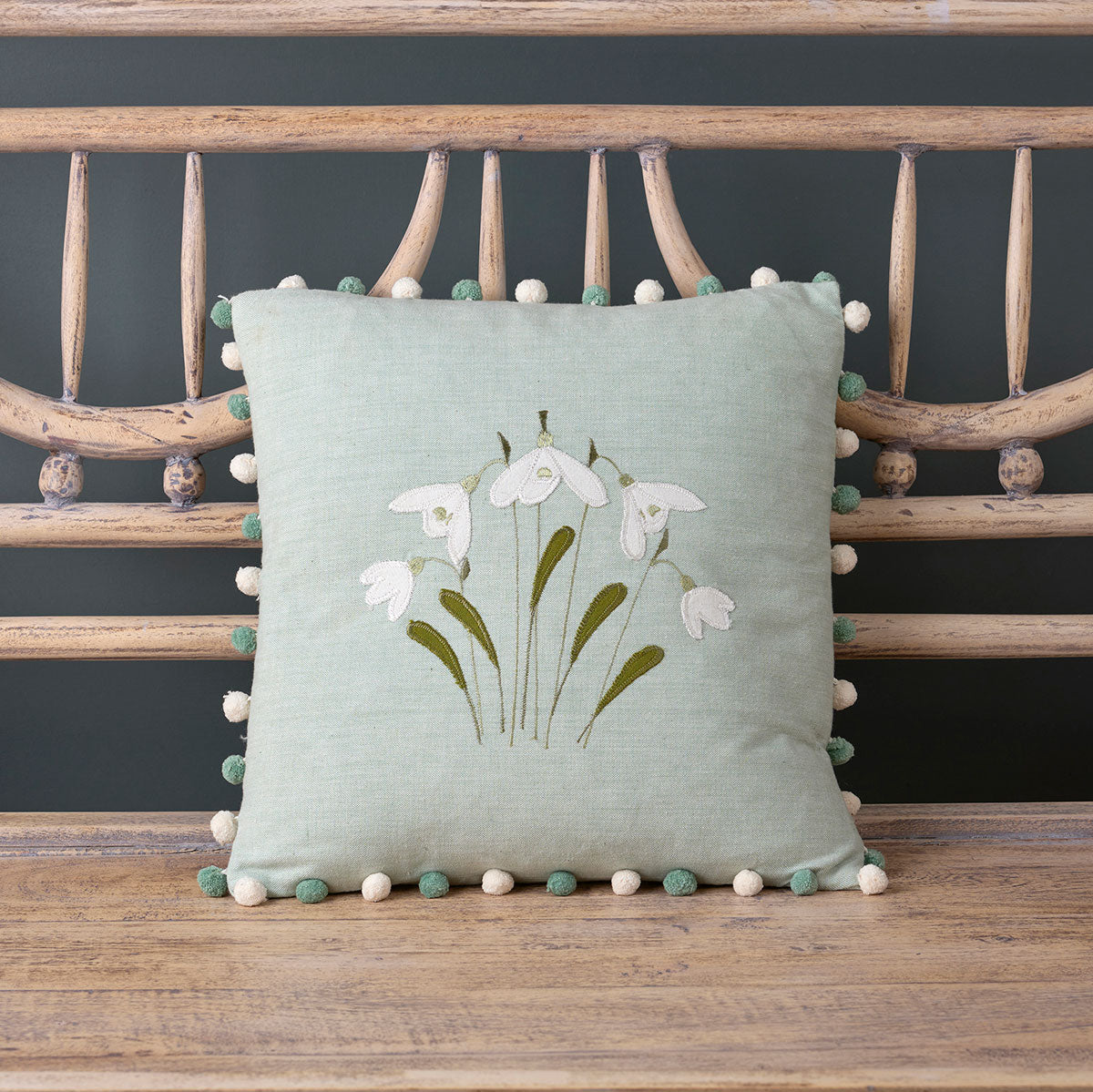 Duck egg snowdrop cushion with pompom trim propped on a bench