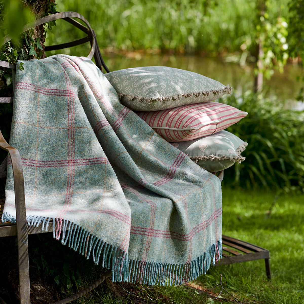Cushions and a woven throw on a garden bench among greenery