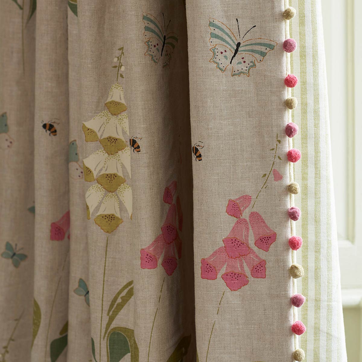 Foxglove linen curtain edged with pink pompom trim beside a plain drape