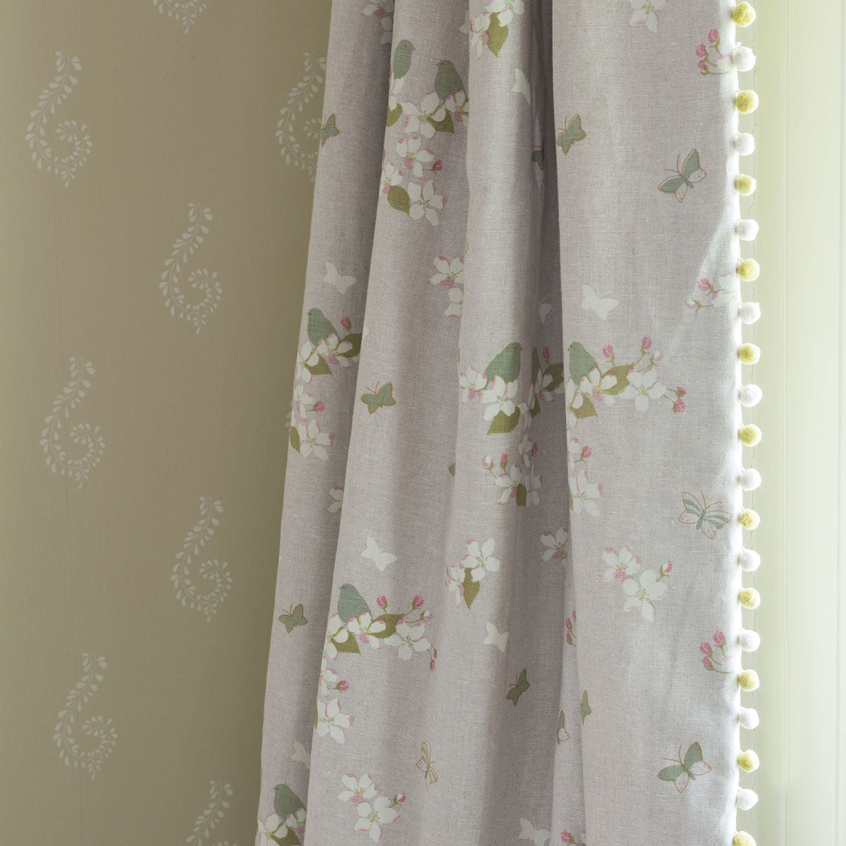 Apple blossom linen curtain with pompom trim against a soft green wall