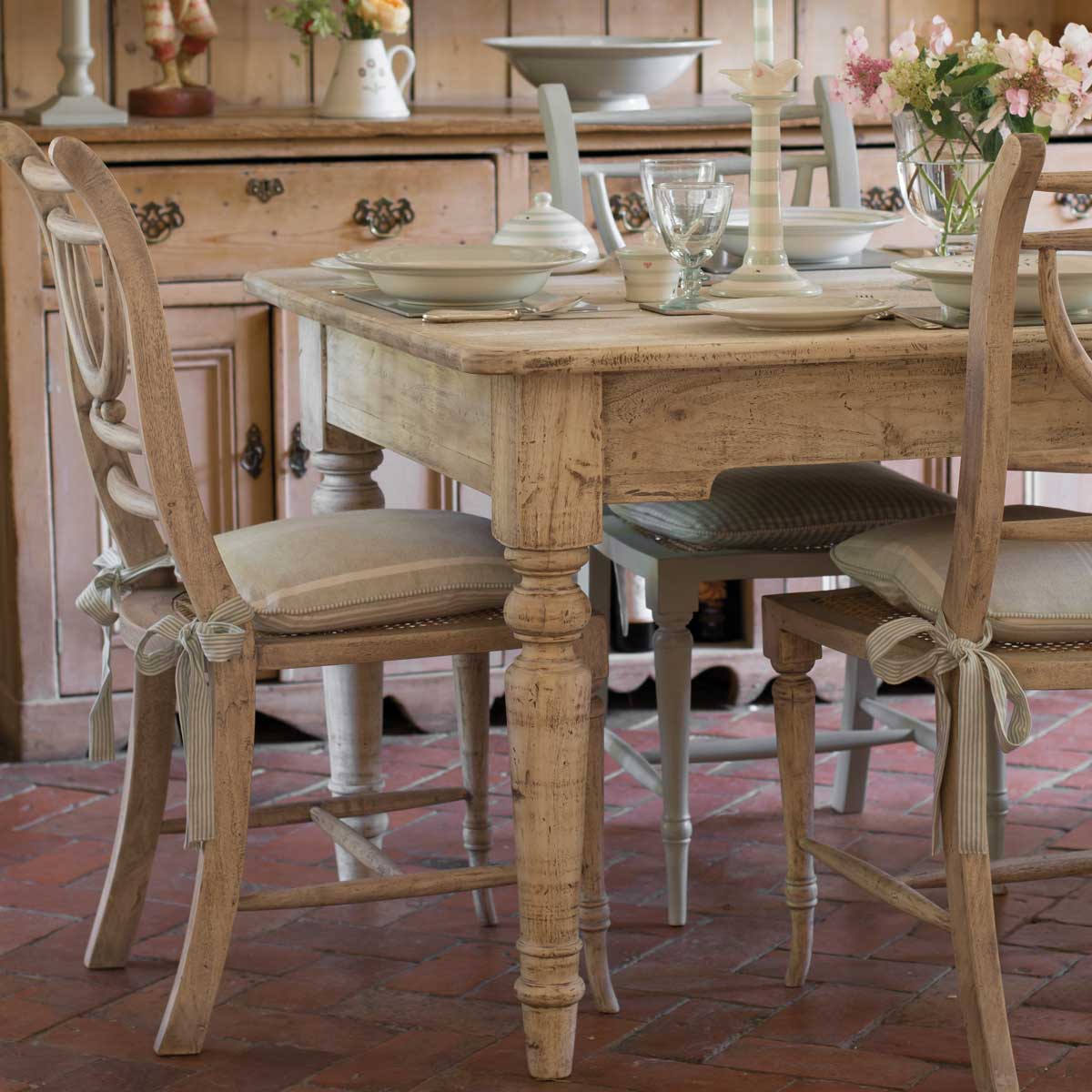 Farmhouse table laid with cream china and painted chairs in daylight