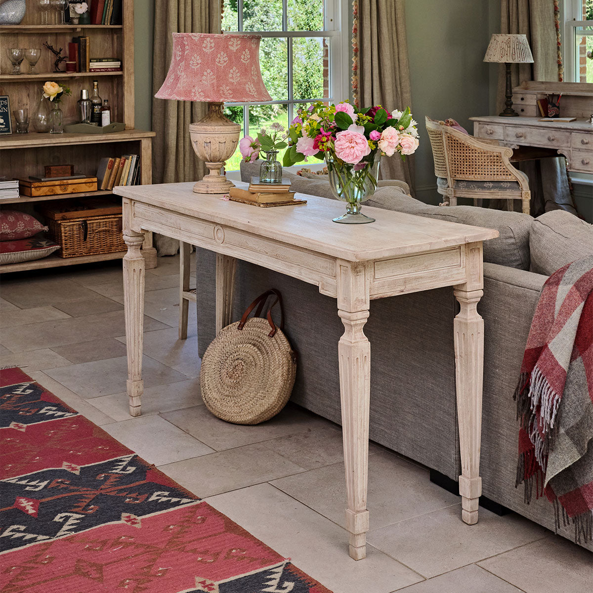 Carved console table behind a sofa with flowers and a kilim rug