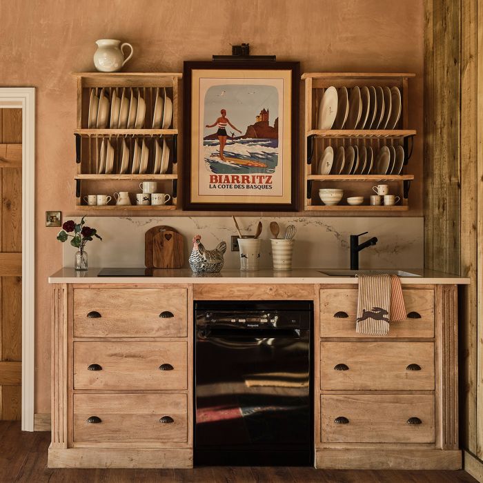 Plate rack above a wooden dresser in a beamed kitchen with mugs and pottery
