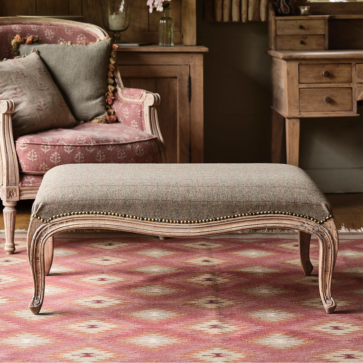 Grey red check tweed upholstering a carved footstool in a book-lined room