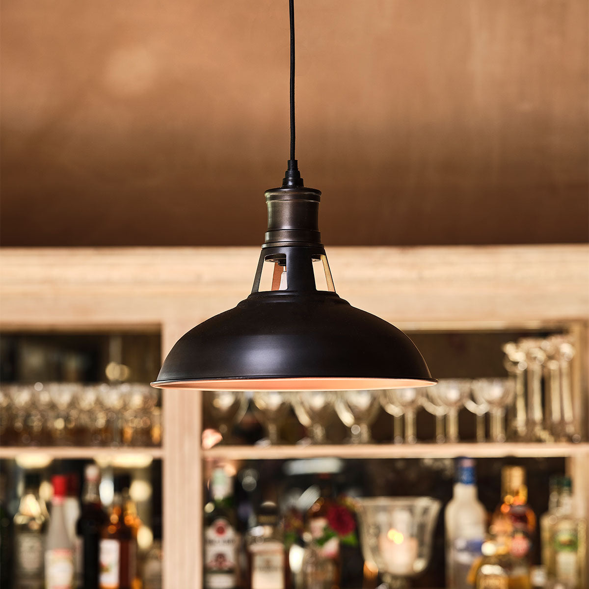 Bronze pendant lamp lighting a bar with glassware and bottles behind