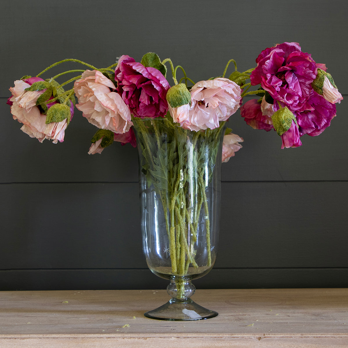 Mixed pink poppies in a tall glass vase against grey panelling