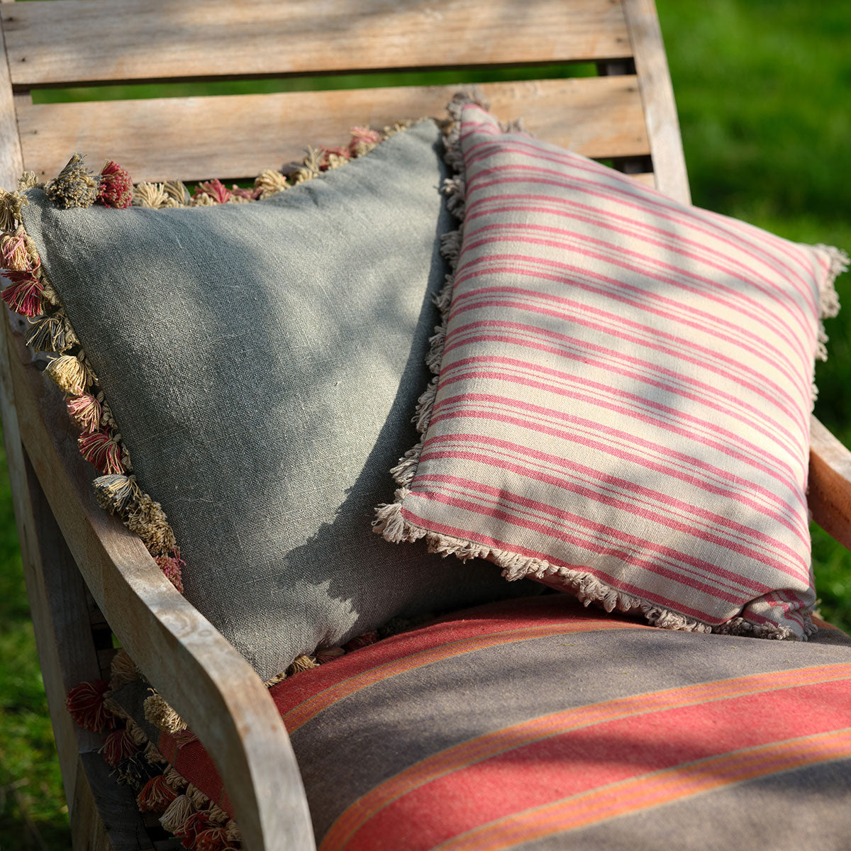 Ticking stripe cushions on a wooden garden bench in soft daylight
