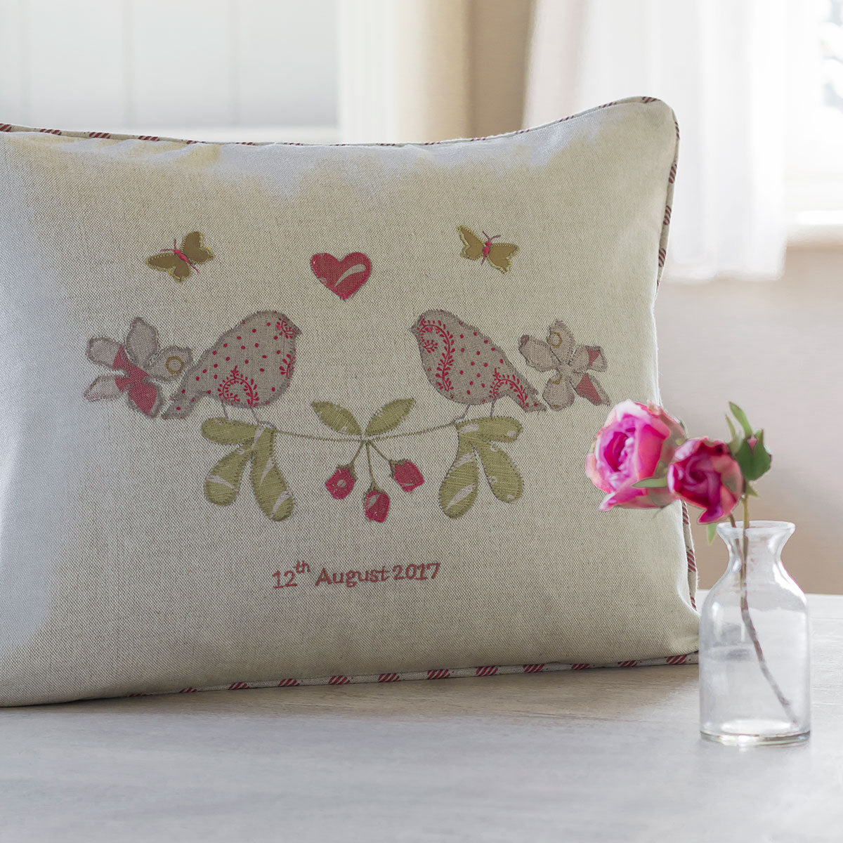 Personalised lovebirds cushion beside a small glass vase of pink roses