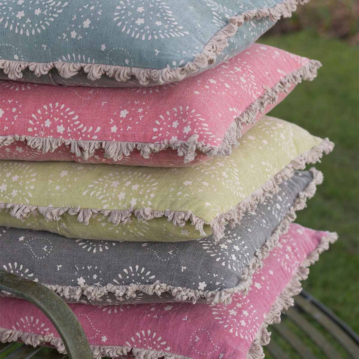 Lullaby cushions in pink, olive, grey and blue stacked on grass