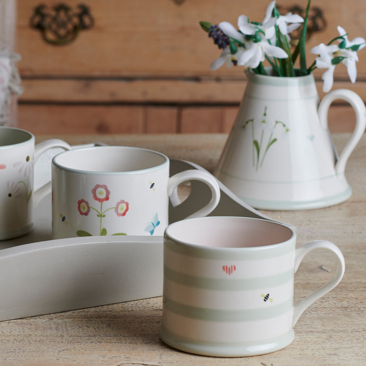 Honey Bees mugs and jug of snowdrops on a wooden dresser
