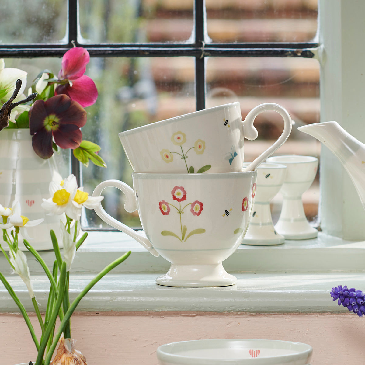 Auricula mugs on a windowsill with primroses and spring flowers