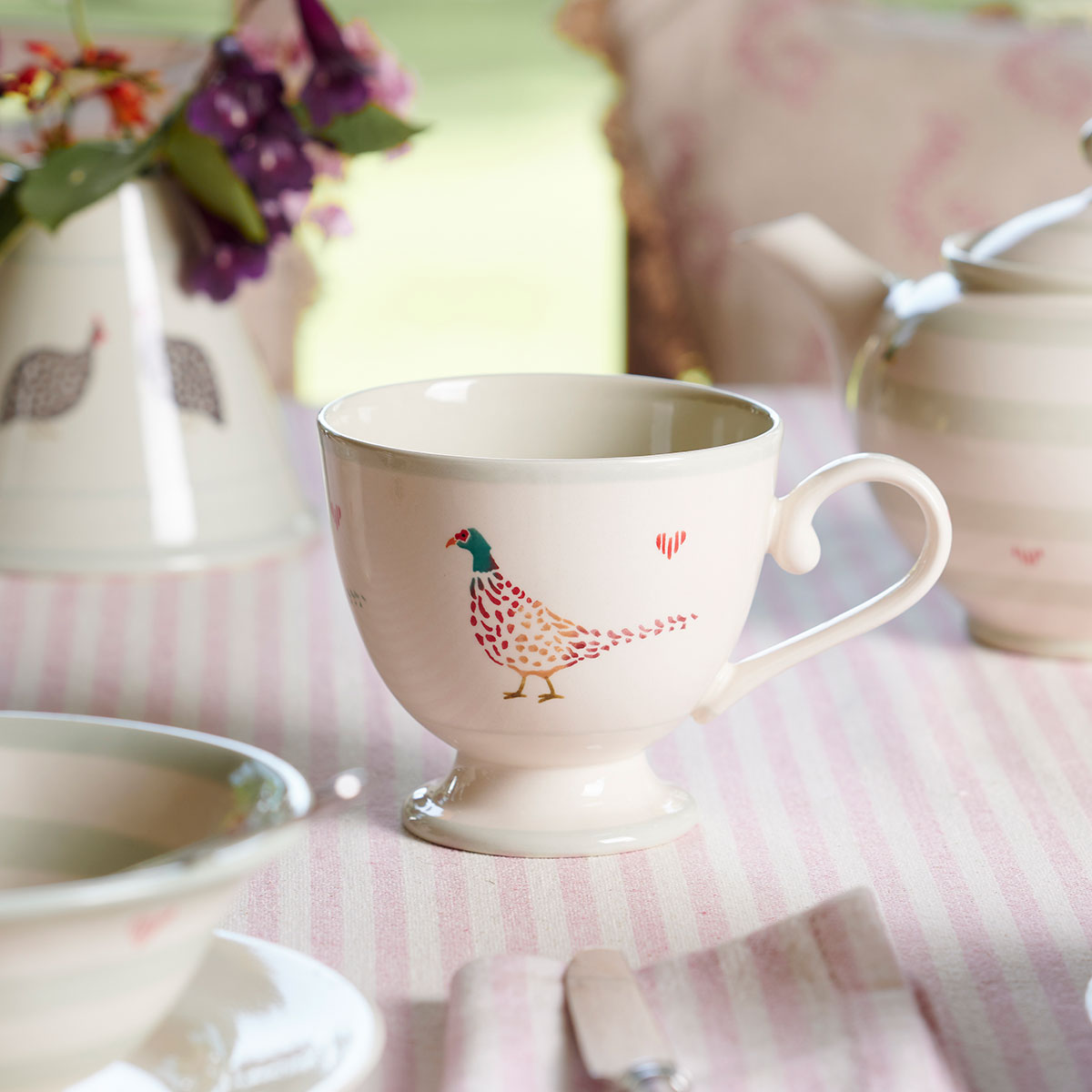 Pheasant mugs and saucers stacked on a pink striped cloth