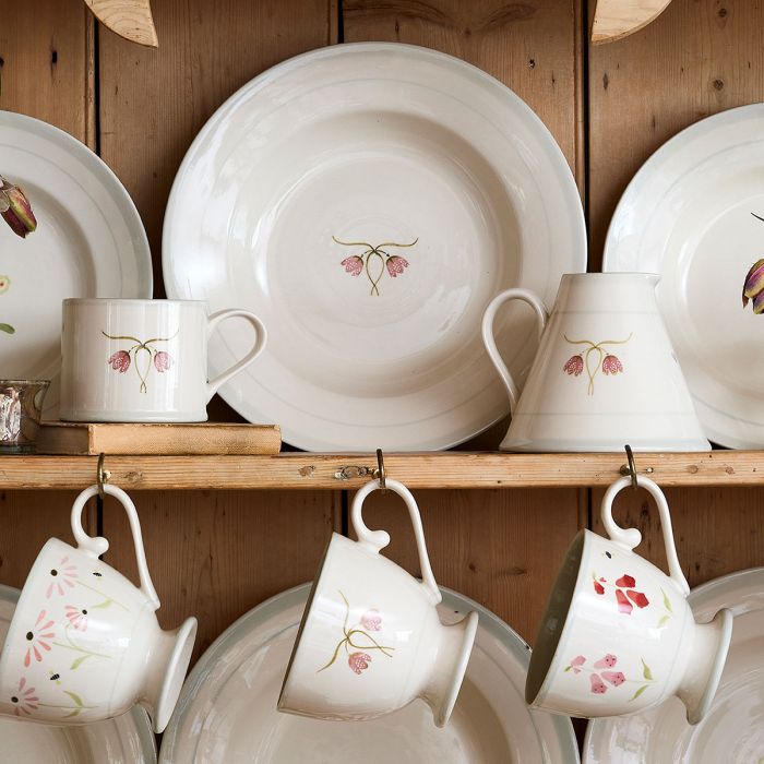 Fritillary plates and mugs stacked on a wooden dresser shelf