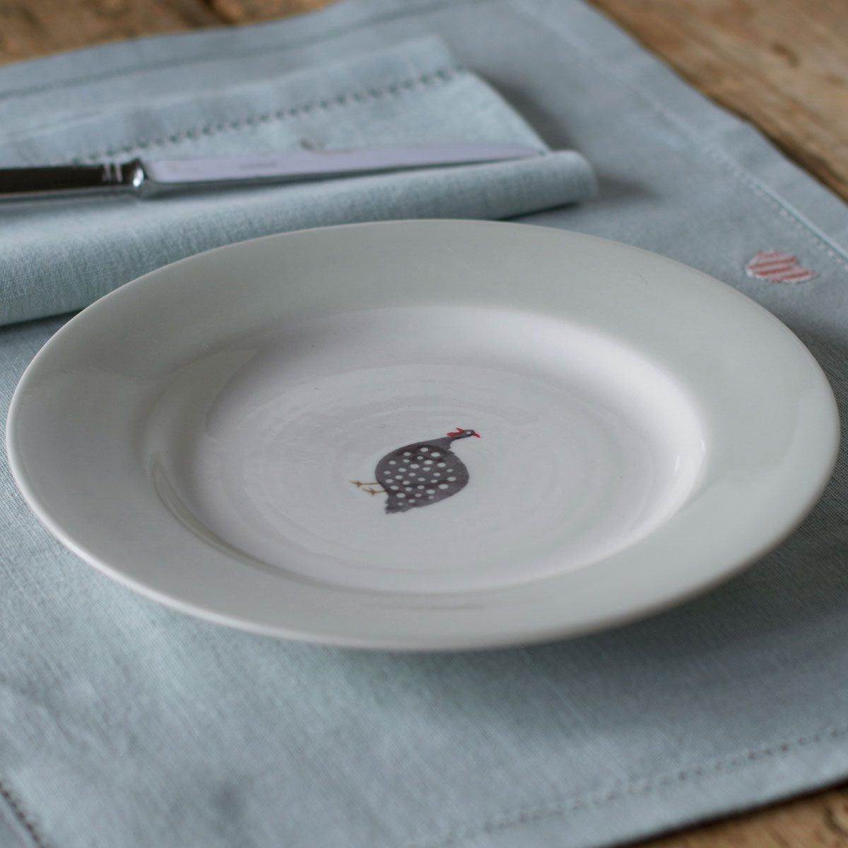 Guinea Fowl side plate with a knife on a pale marble surface