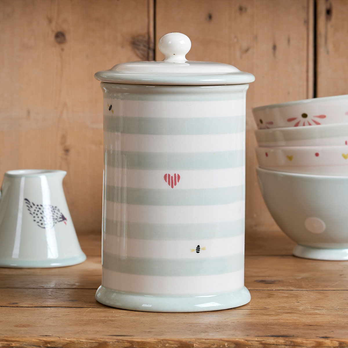 Honey Bees storage jar with sage stripes and painted heart on a wooden shelf
