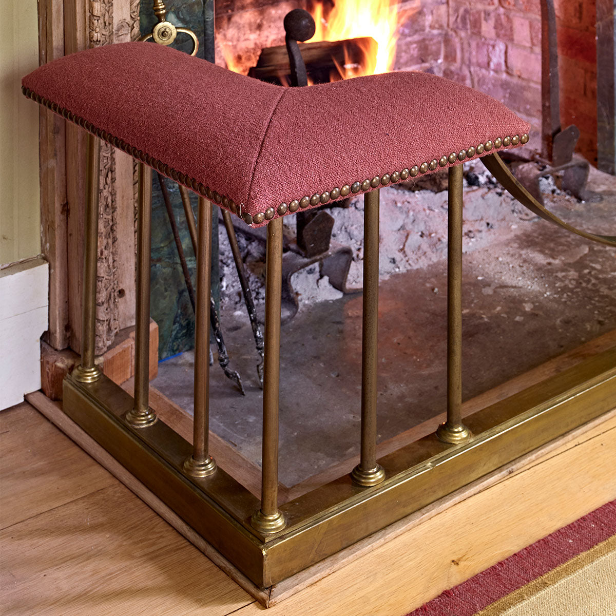 Corner view of a red velvet fire fender with brass rails and open fire
