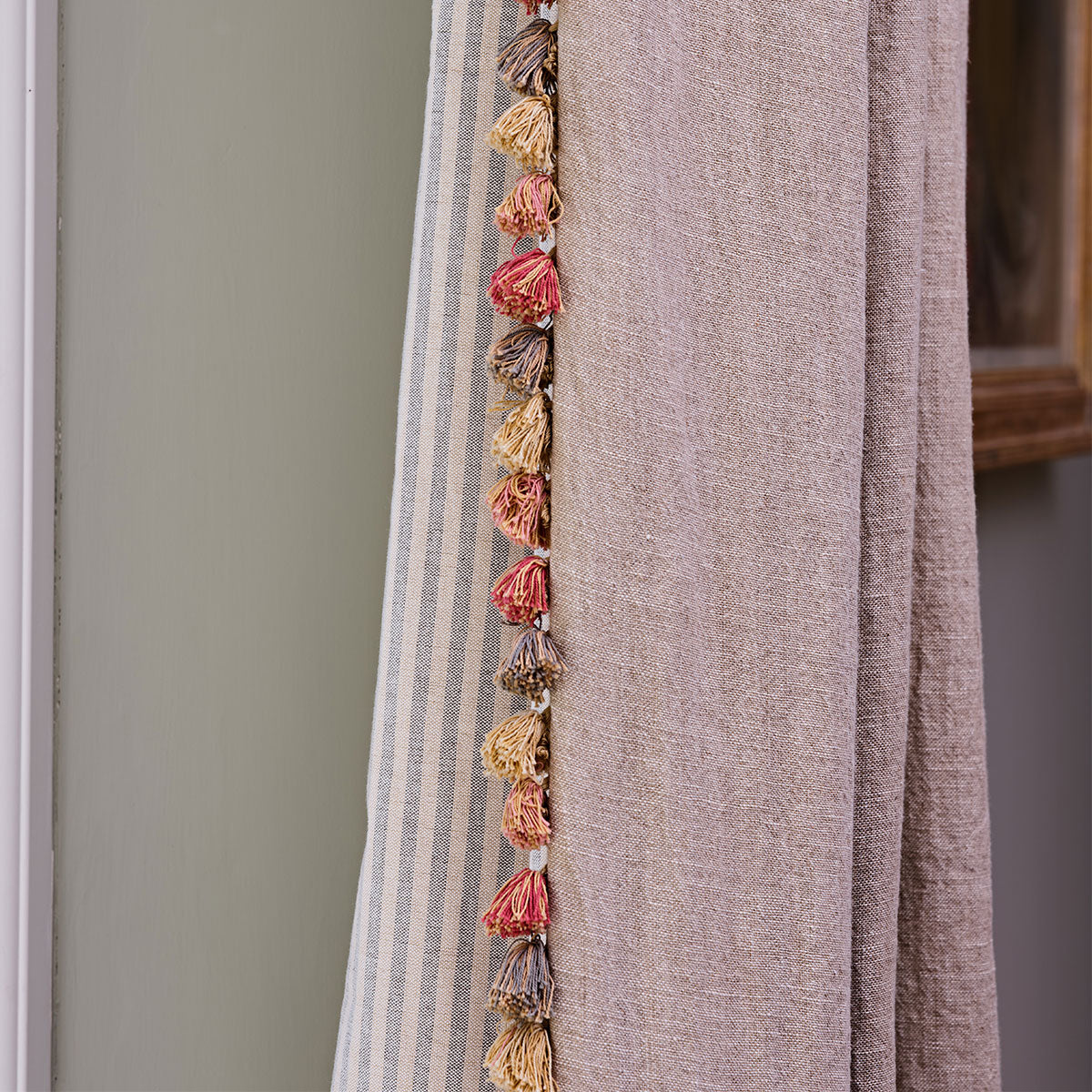 Light rustic linen curtain with pom pom trim layered against a pink curtain