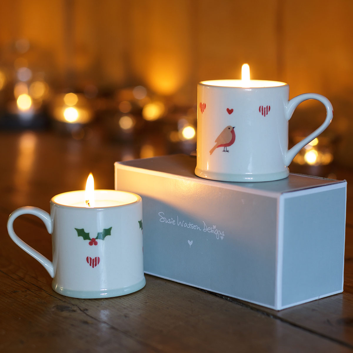Lit scented candles in espresso mugs beside their pale gift box