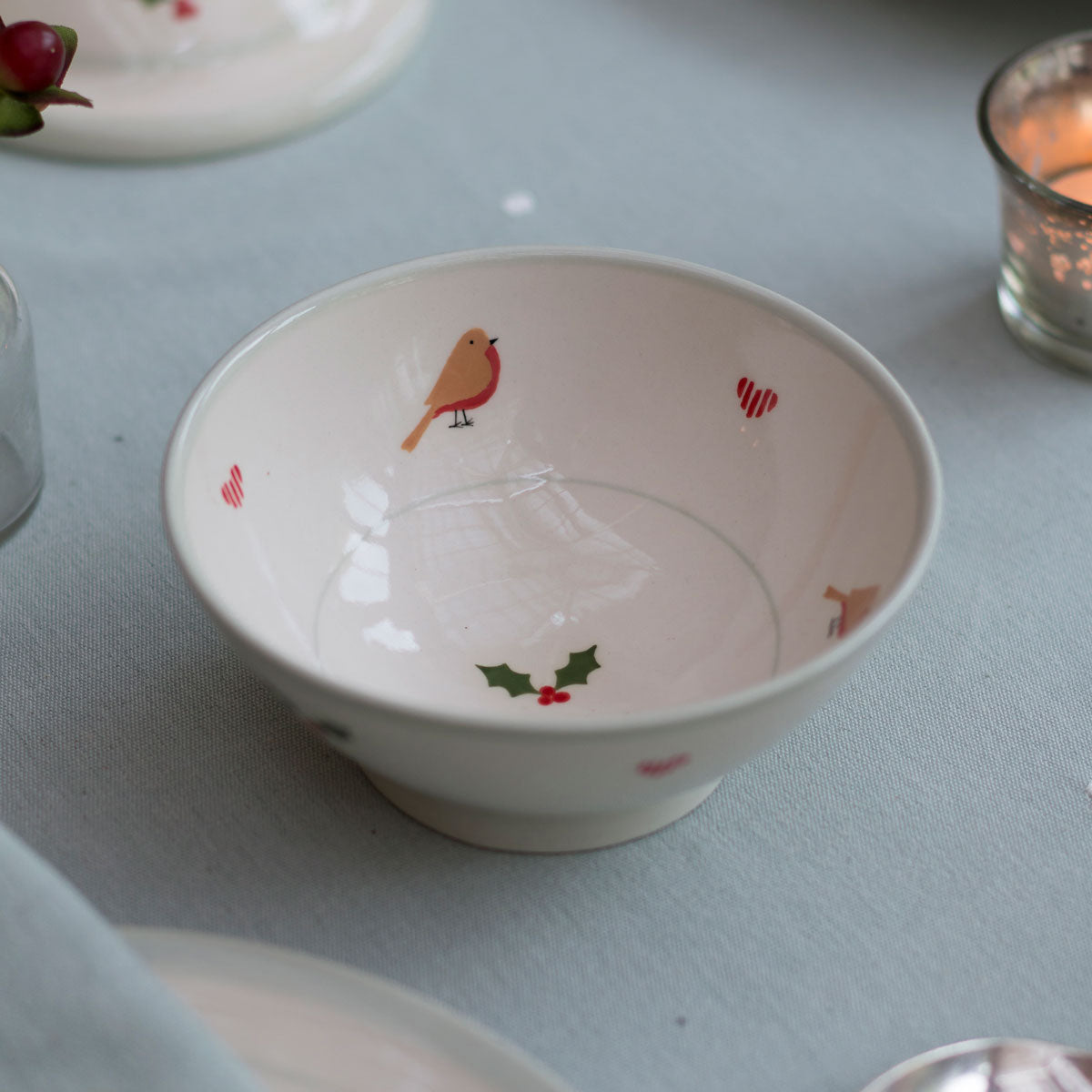Christmas robin small bowl with holly sprigs on a pale table