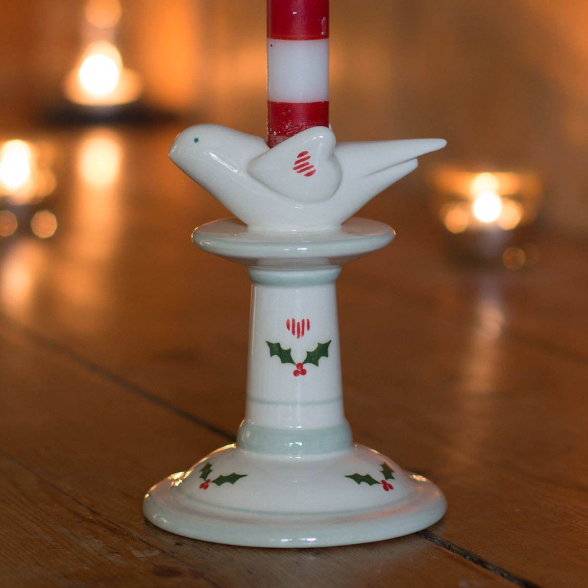 Small Christmas bird candlestick with holly motif, candlelight glowing behind