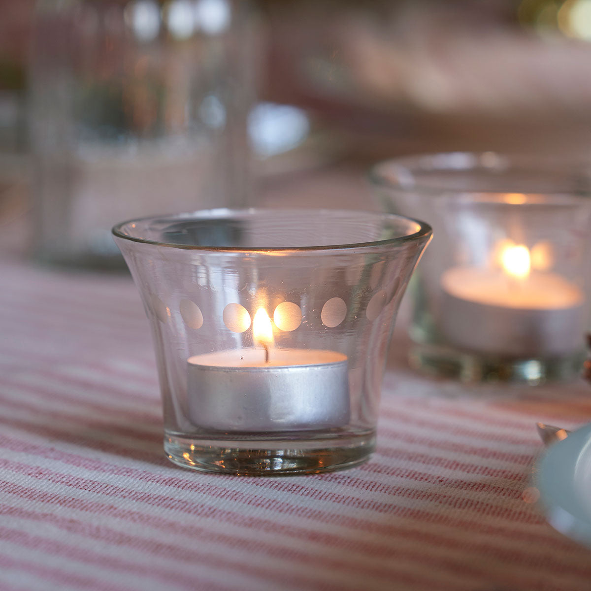 Two glass candlepots burning on a pink striped table