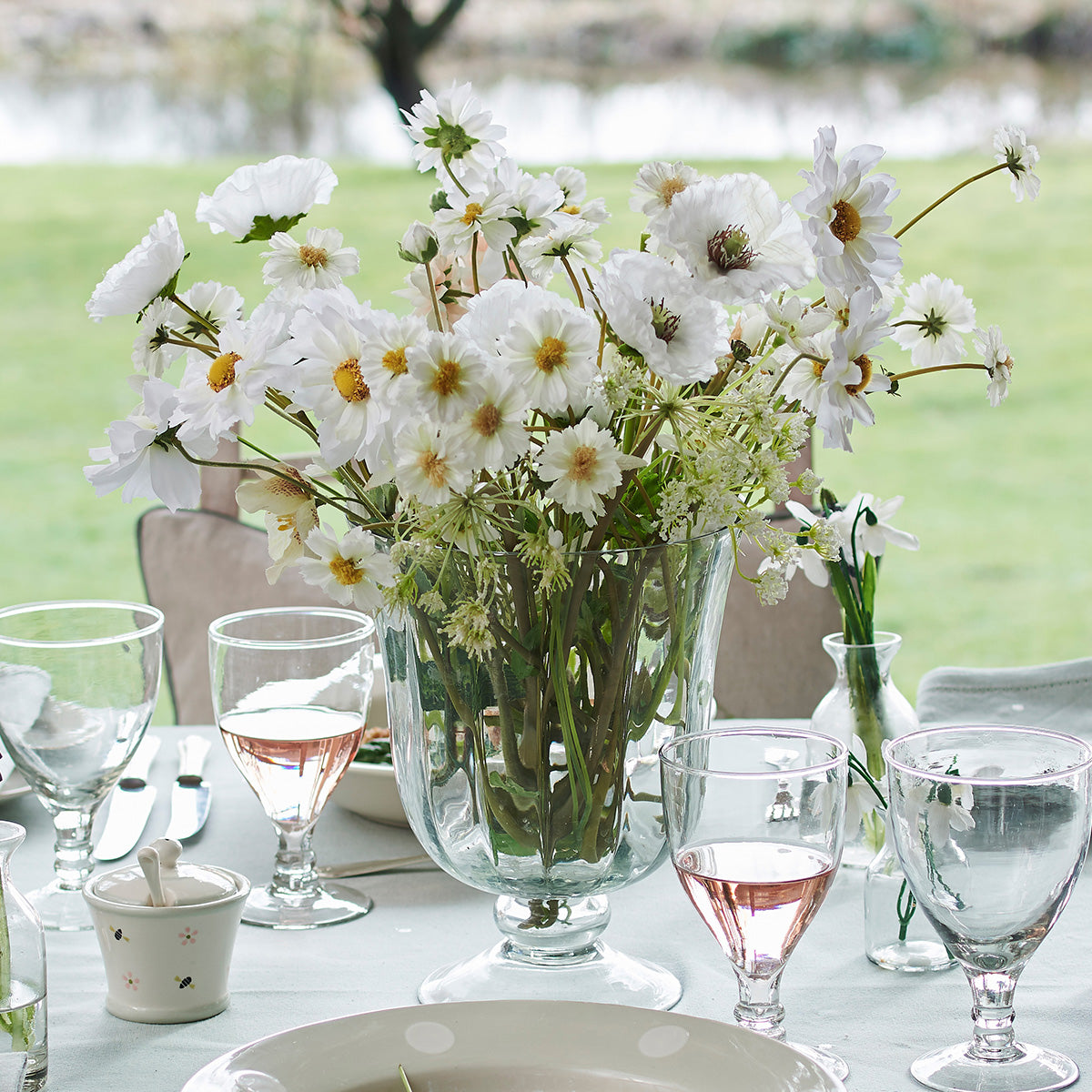 Hurricane vase filled with white cosmos on a table laid outdoors