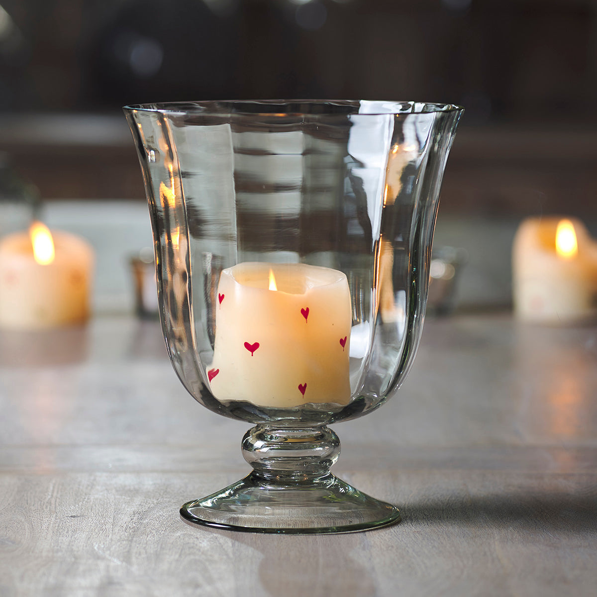Sculpted glass hurricane vase holding a lit painted candle on a table