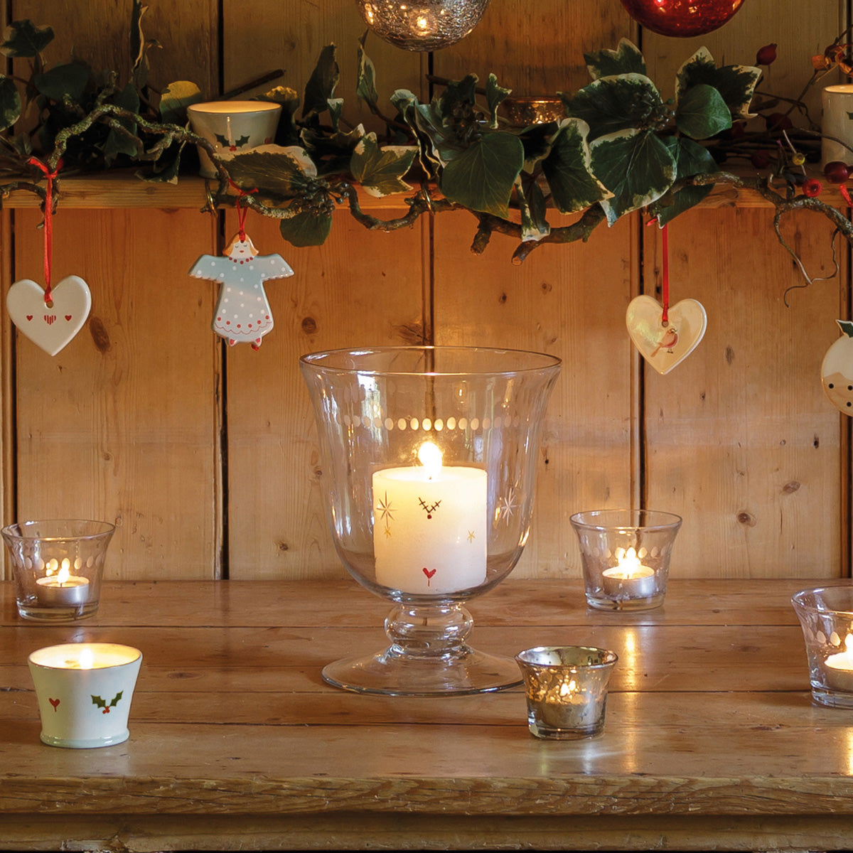Candle in a hurricane below hanging heart decorations, tealights alongside