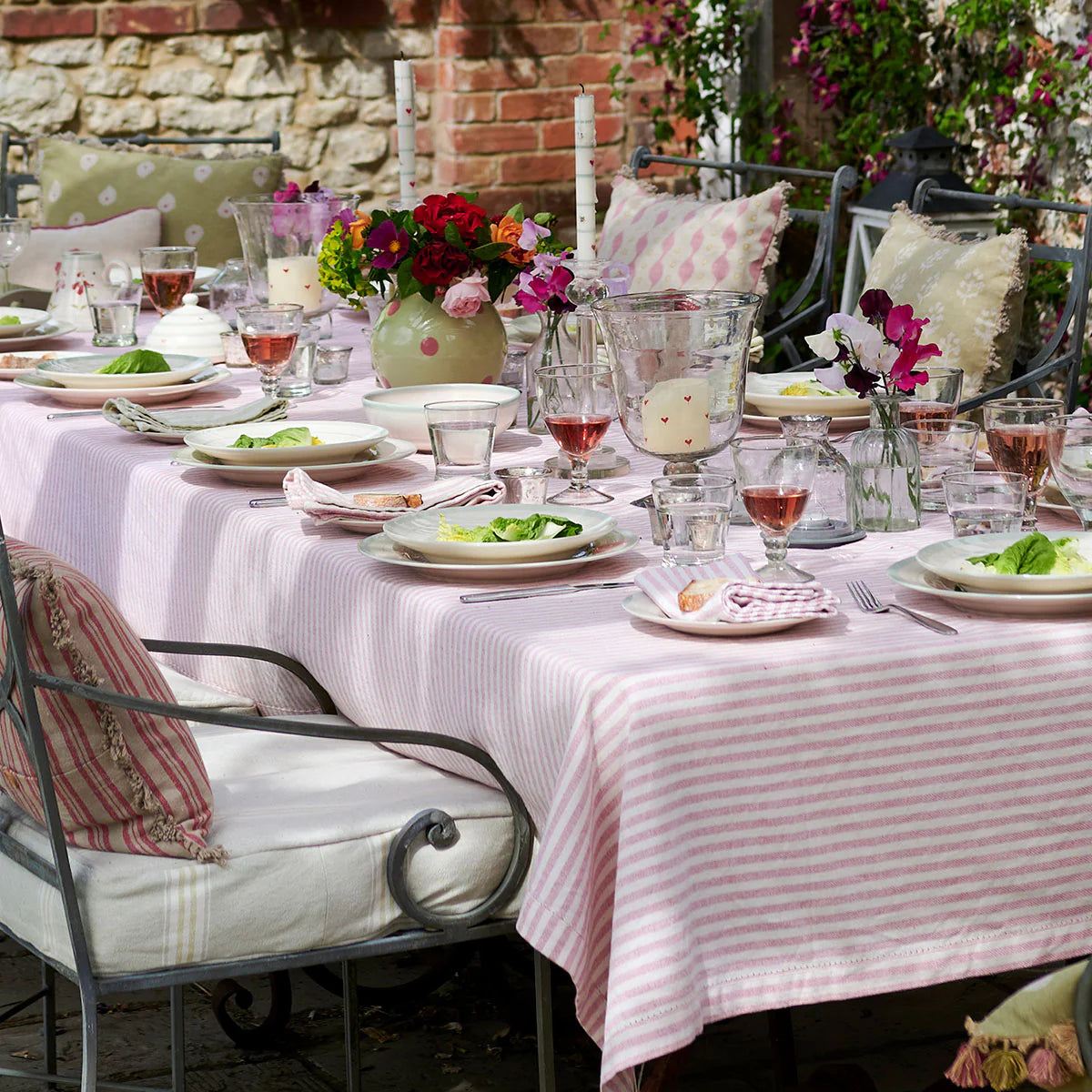 Striped tablecloth on a long table laid outdoors with flowers and glasses