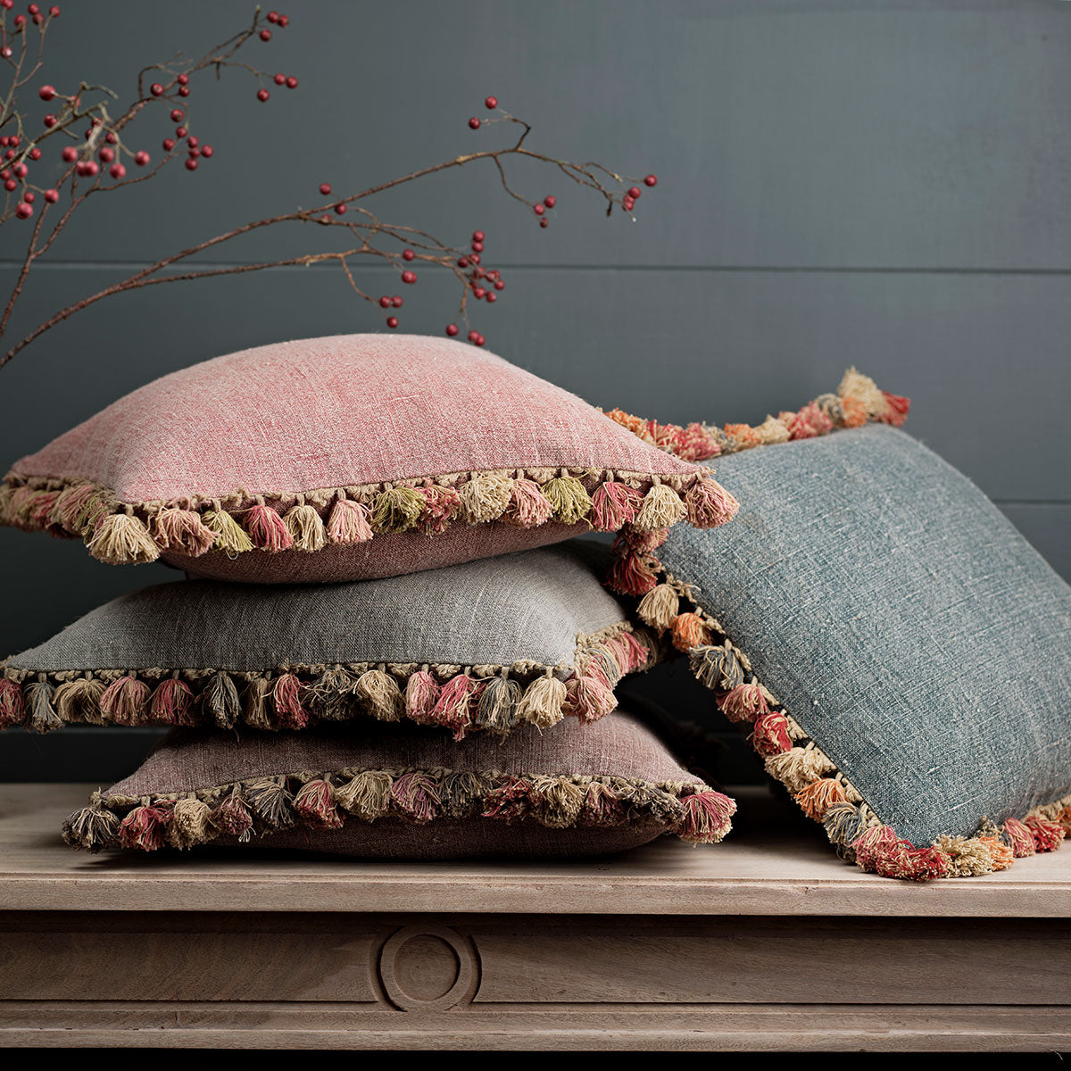 Faded indigo cushion stacked with dusky pink linen cushions and tassel trims