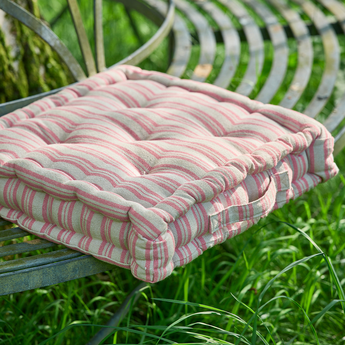 Rusty rose ticking stripe box cushion resting on a curved metal garden bench