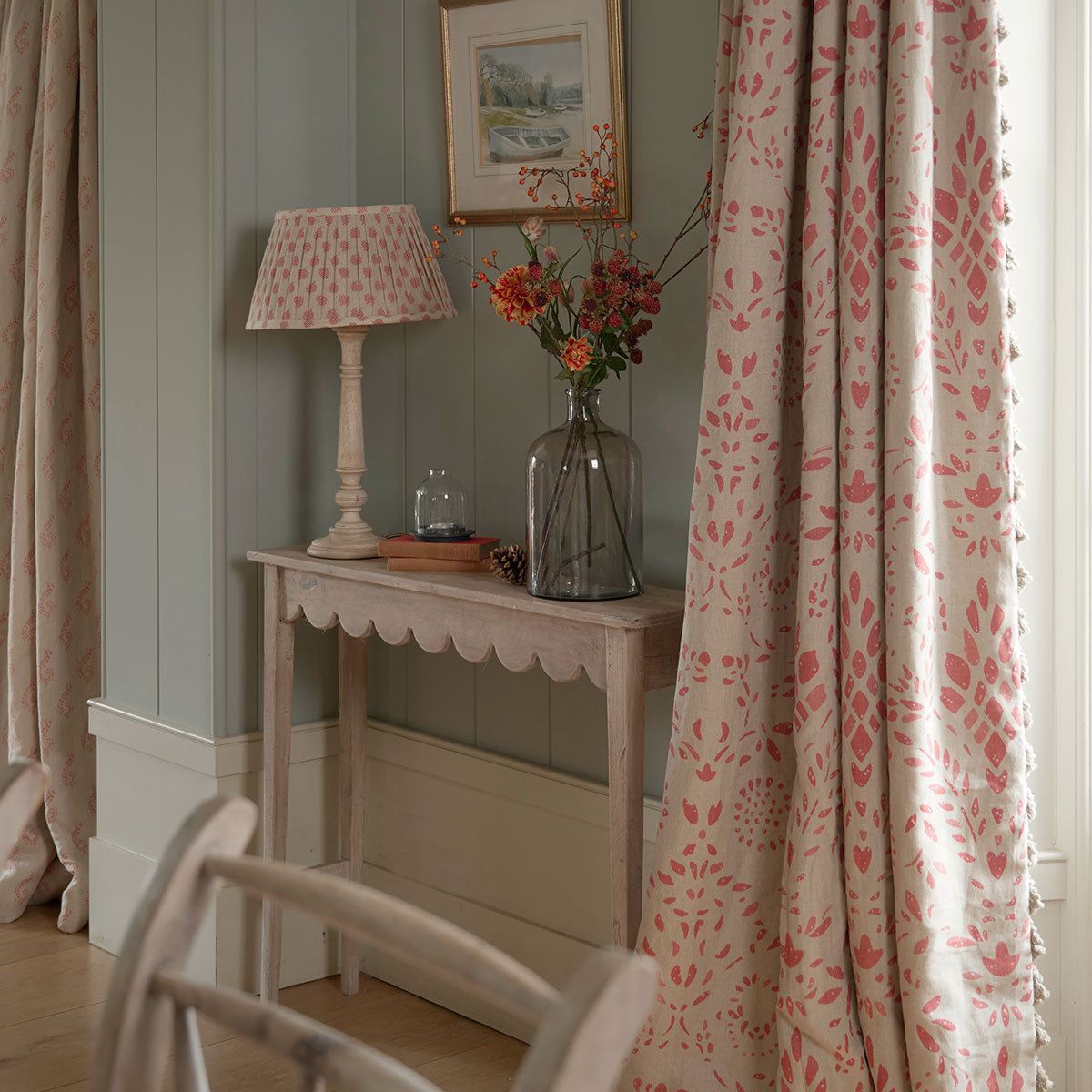 Scalloped table with a lamp and flowers beside patterned curtains