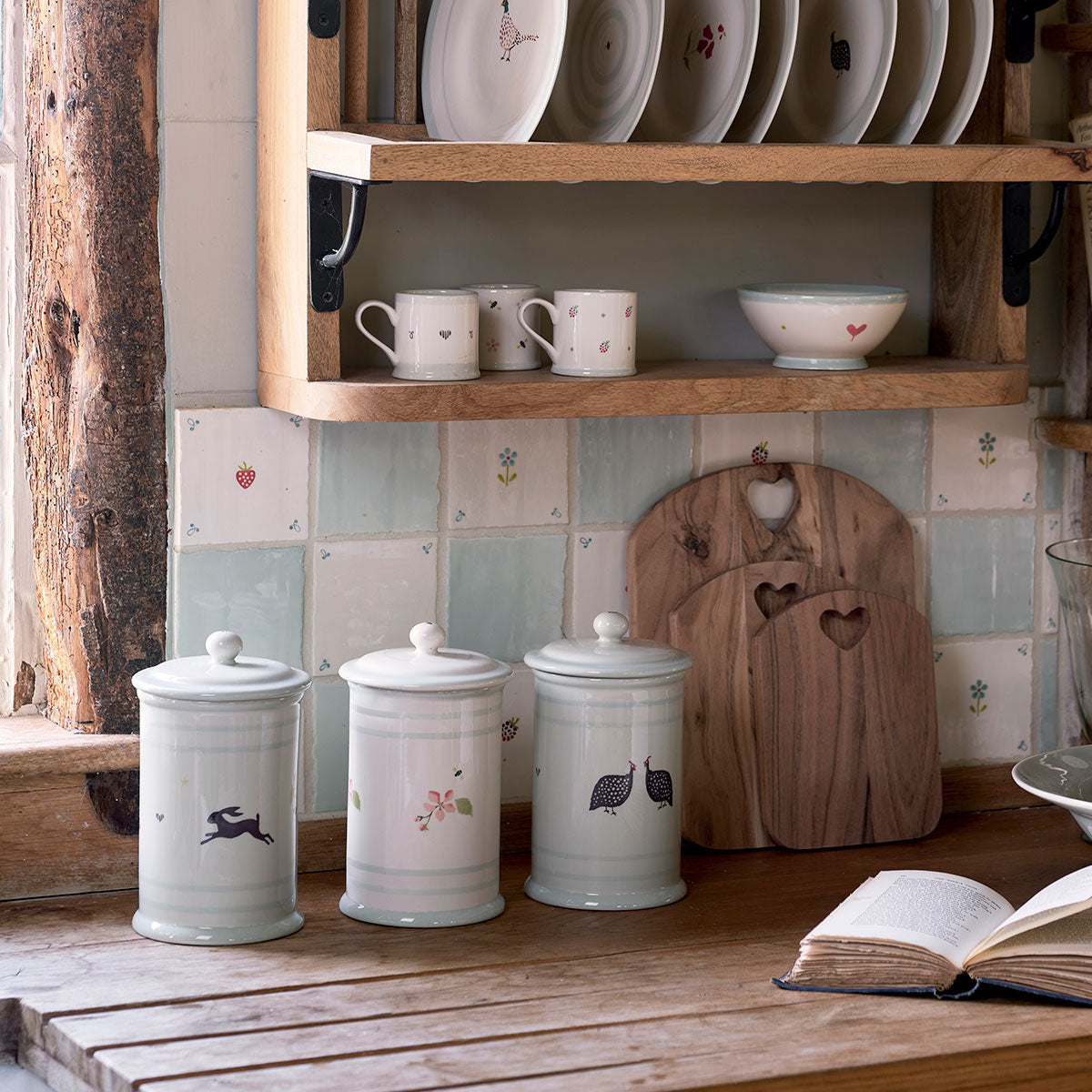Row of storage jars on a kitchen shelf with china and boards